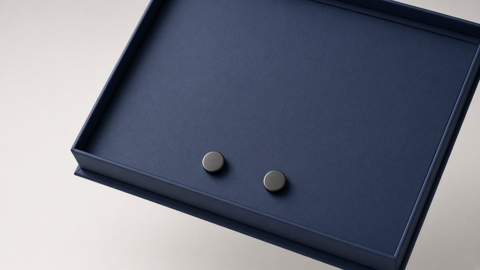 Two round magnets placed side by side inside an open navy box lid near the opening edge